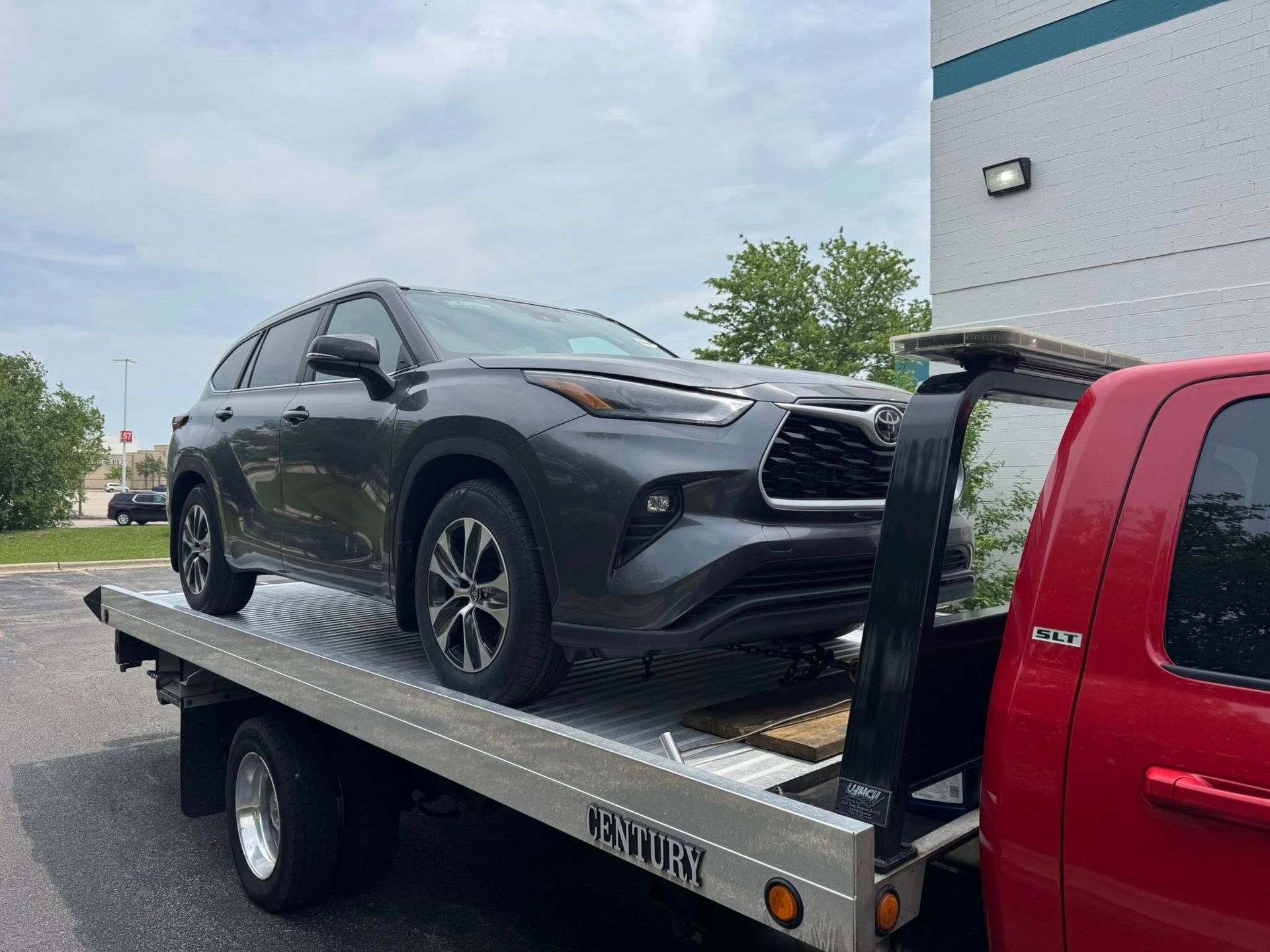 Dark gray Toyota Highlander on a flatbed tow truck, outdoors near a building.
