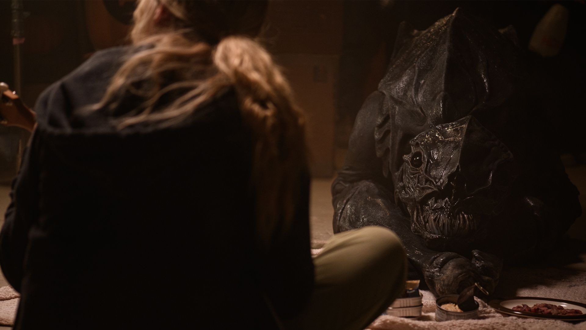 A woman is sitting on the floor looking at a monster.