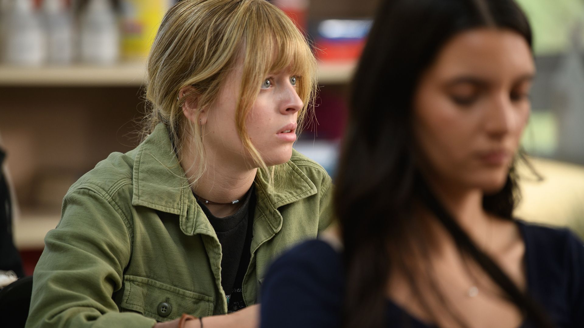A woman in a green jacket is sitting next to another woman in a classroom.