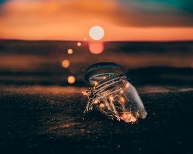 A jar filled with lights is sitting on the ground at sunset.