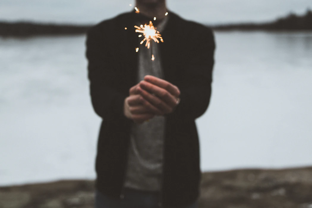 A man in a black jacket is holding a sparkler in his hands