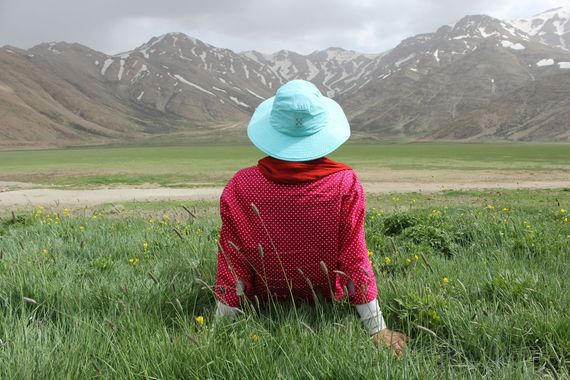 A woman in a blue hat sits in a field with mountains in the background