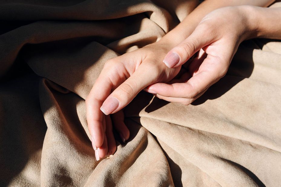 Le mani di una donna sono appoggiate su una coperta marrone chiaro.