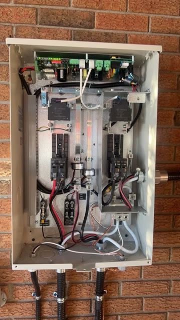 The inside of a electrical box is hanging on a brick wall.