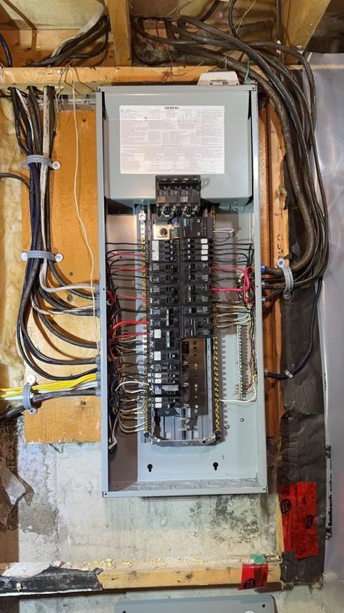 A electrical panel is hanging on a wall in a basement.