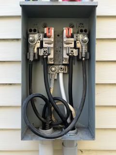 A close up of an electrical box on the side of a house with wires coming out of it.
