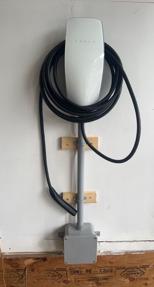 A tesla charging station is attached to a wall in a garage.