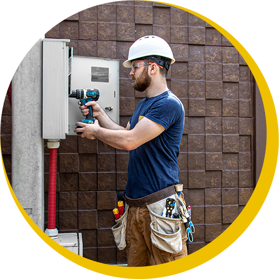 A man wearing a hard hat is working on a box with a drill.