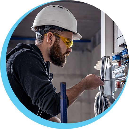 A man wearing a hard hat and safety glasses is working on an electrical box.