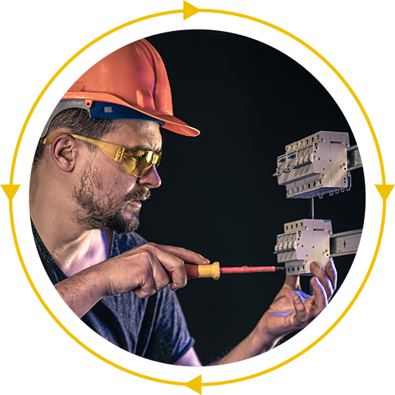 A man wearing a hard hat and safety glasses is working on an electrical box with a screwdriver.