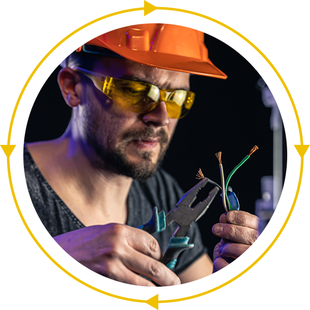 A man wearing a hard hat and safety glasses is holding a pair of pliers