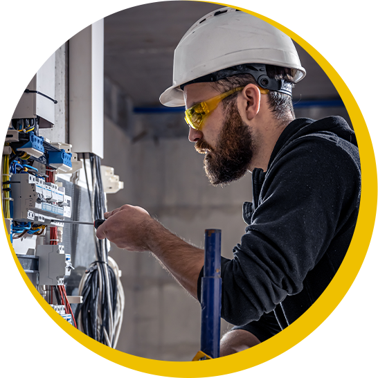 A man wearing a hard hat and goggles is working on an electrical box.