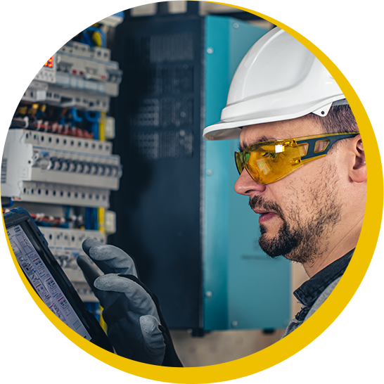 A man wearing a hard hat and safety glasses is looking at a tablet