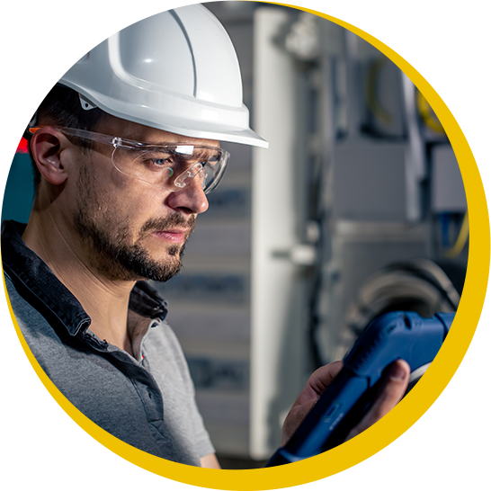 A man wearing a hard hat and glasses is looking at a tablet