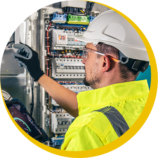 A man wearing a hard hat and safety vest is working on an electrical box.