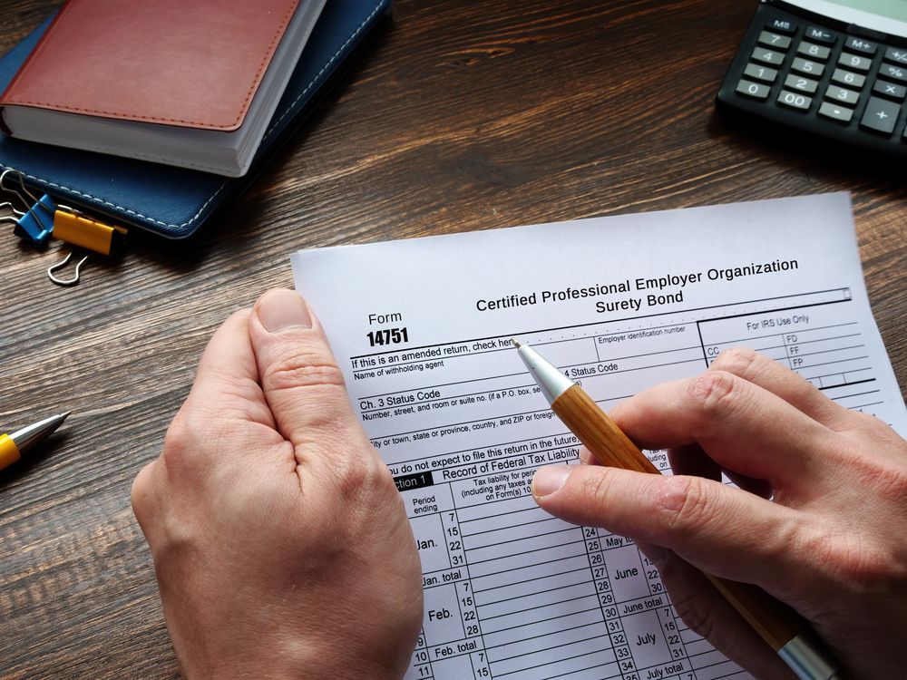 Hands holding a pen over a tax form on a wooden desk with office supplies nearby.
