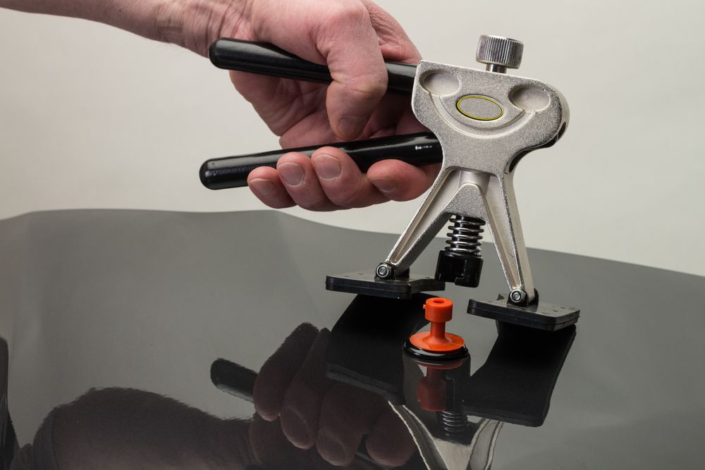A person using a dent repair tool on a black car surface.