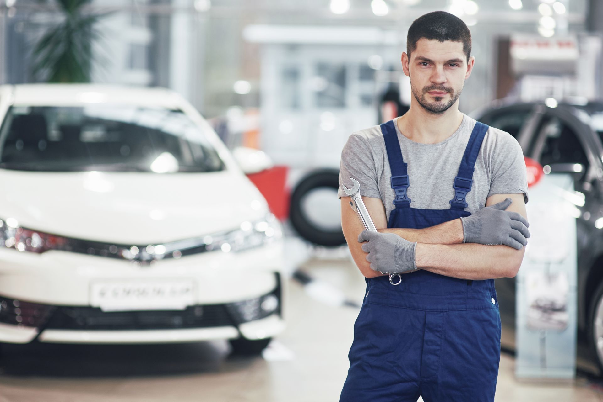 A man in overalls is standing in front of a car in a showroom.