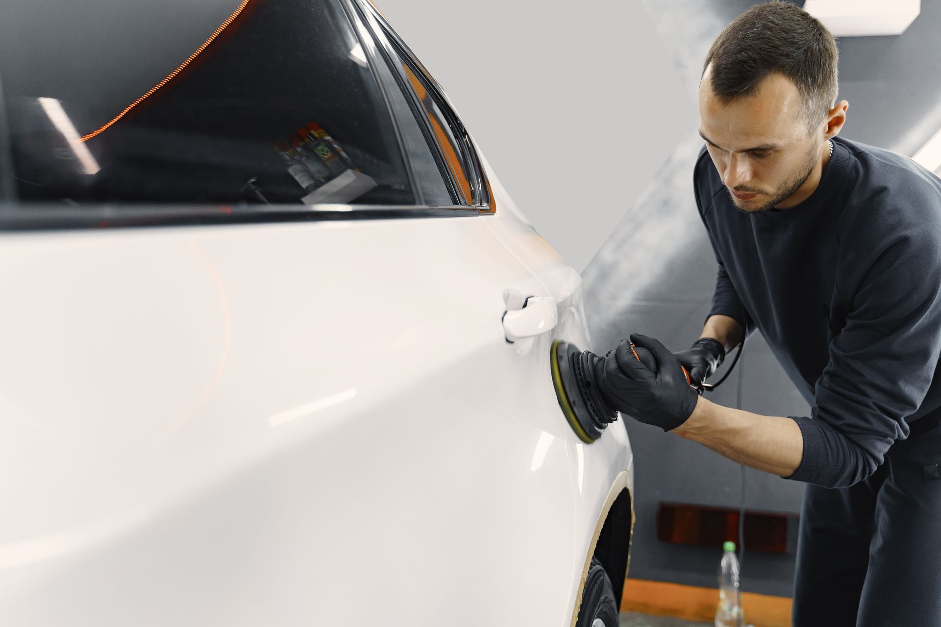 A man is polishing a white car with a machine.