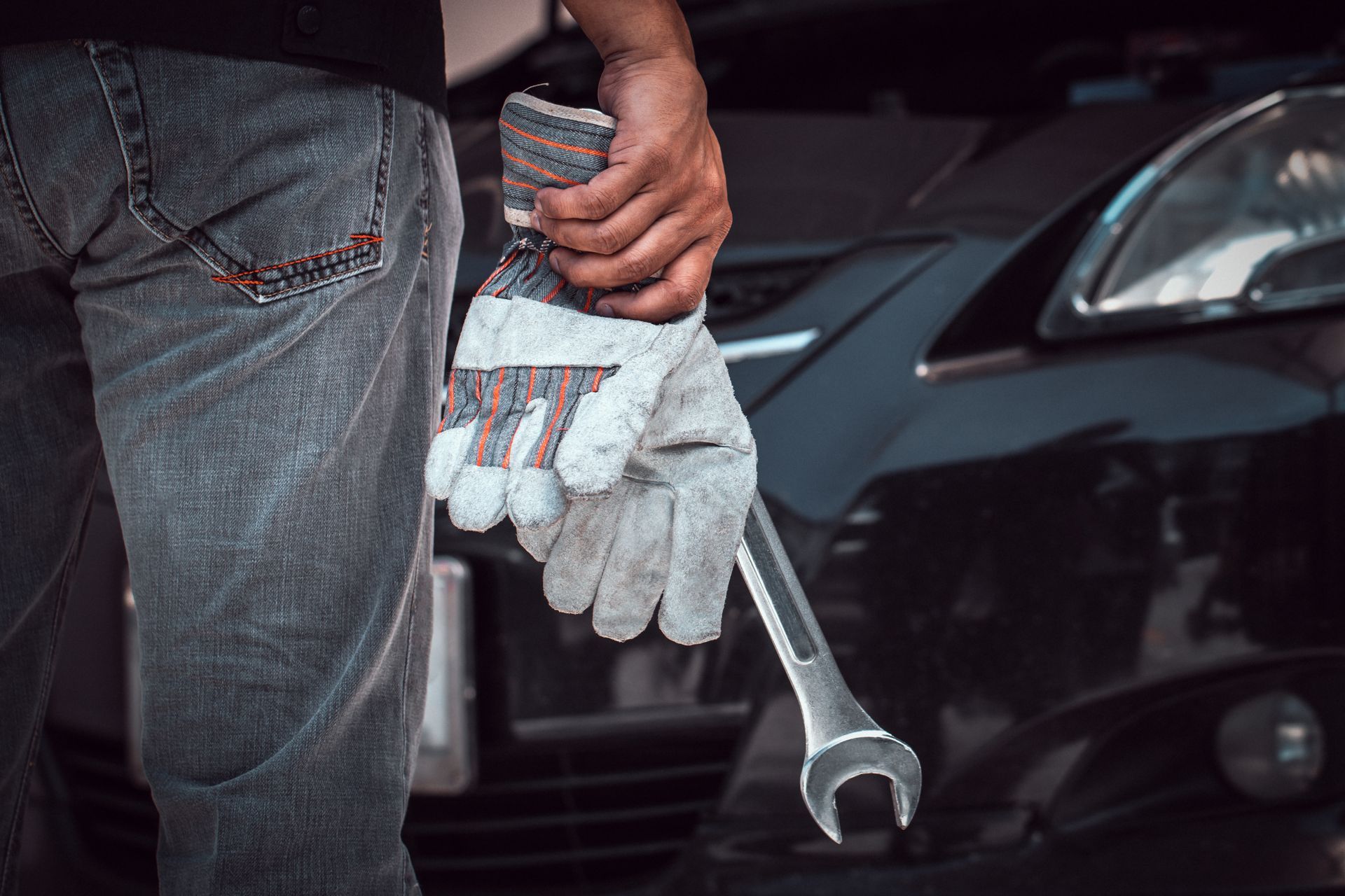 A man is holding a wrench and a pair of gloves in front of a car.