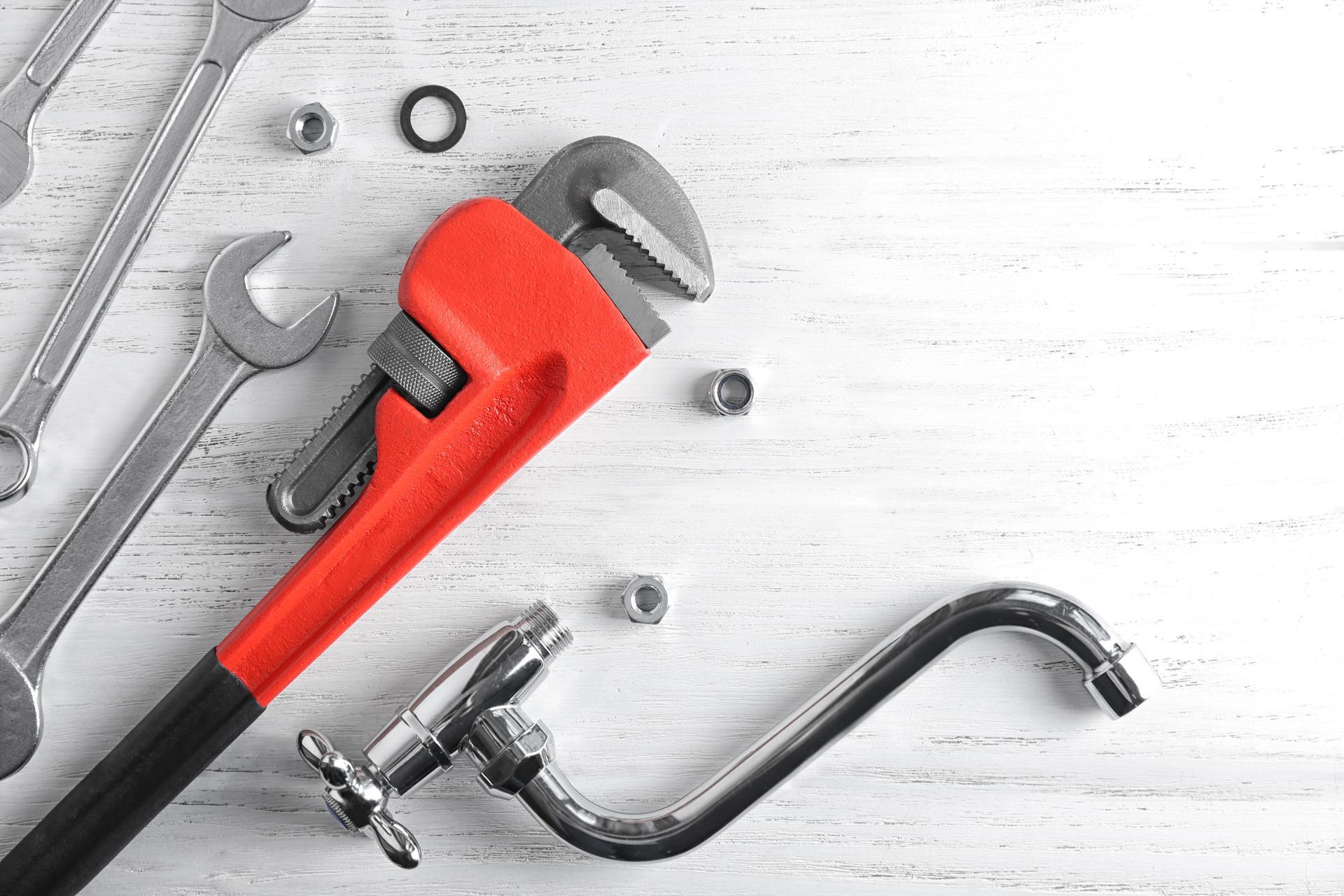A wrench and a faucet are on a white wooden table.
