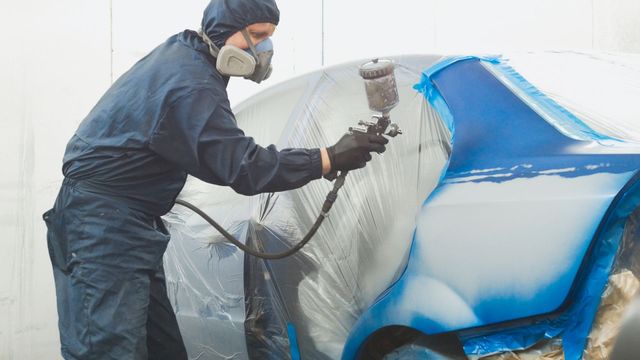 a man wearing a mask is spray painting a car .