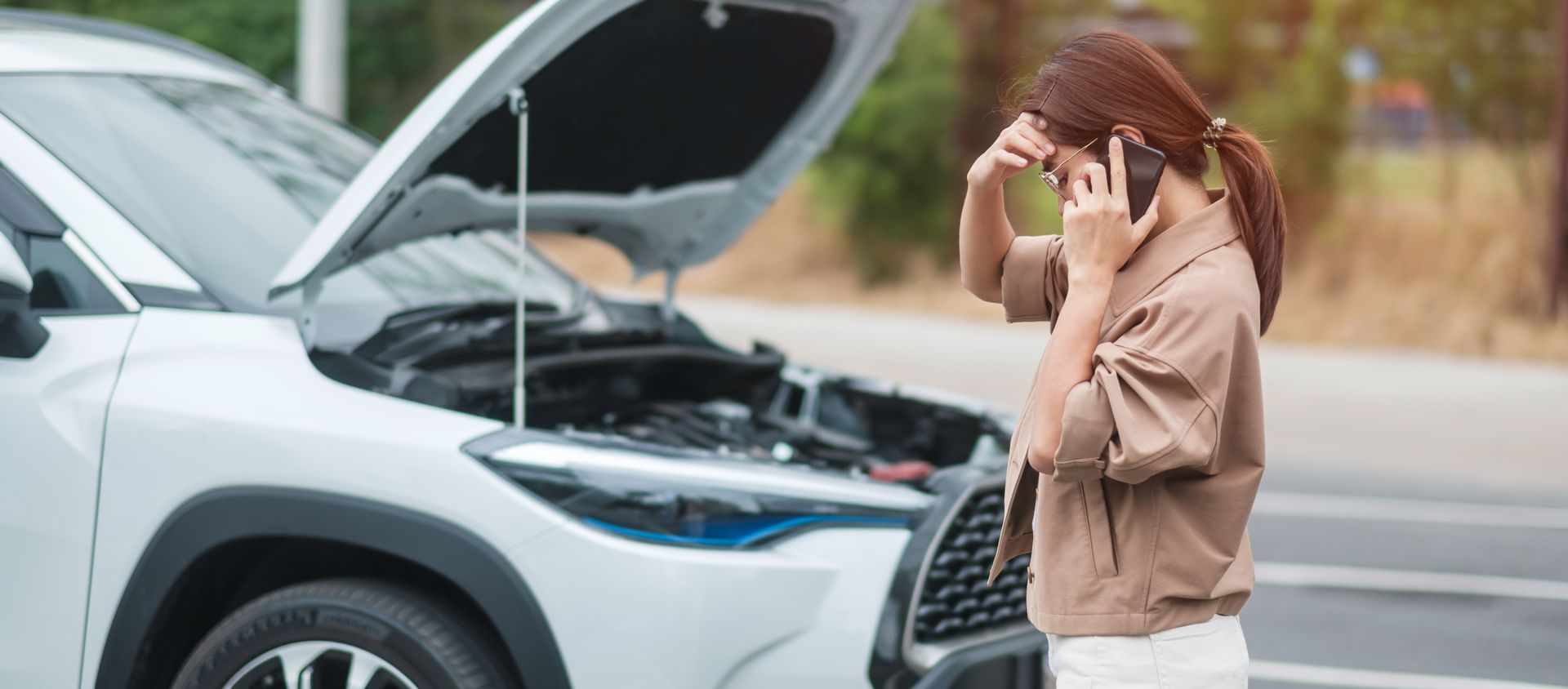 A woman is talking on a cell phone in front of a broken down car.