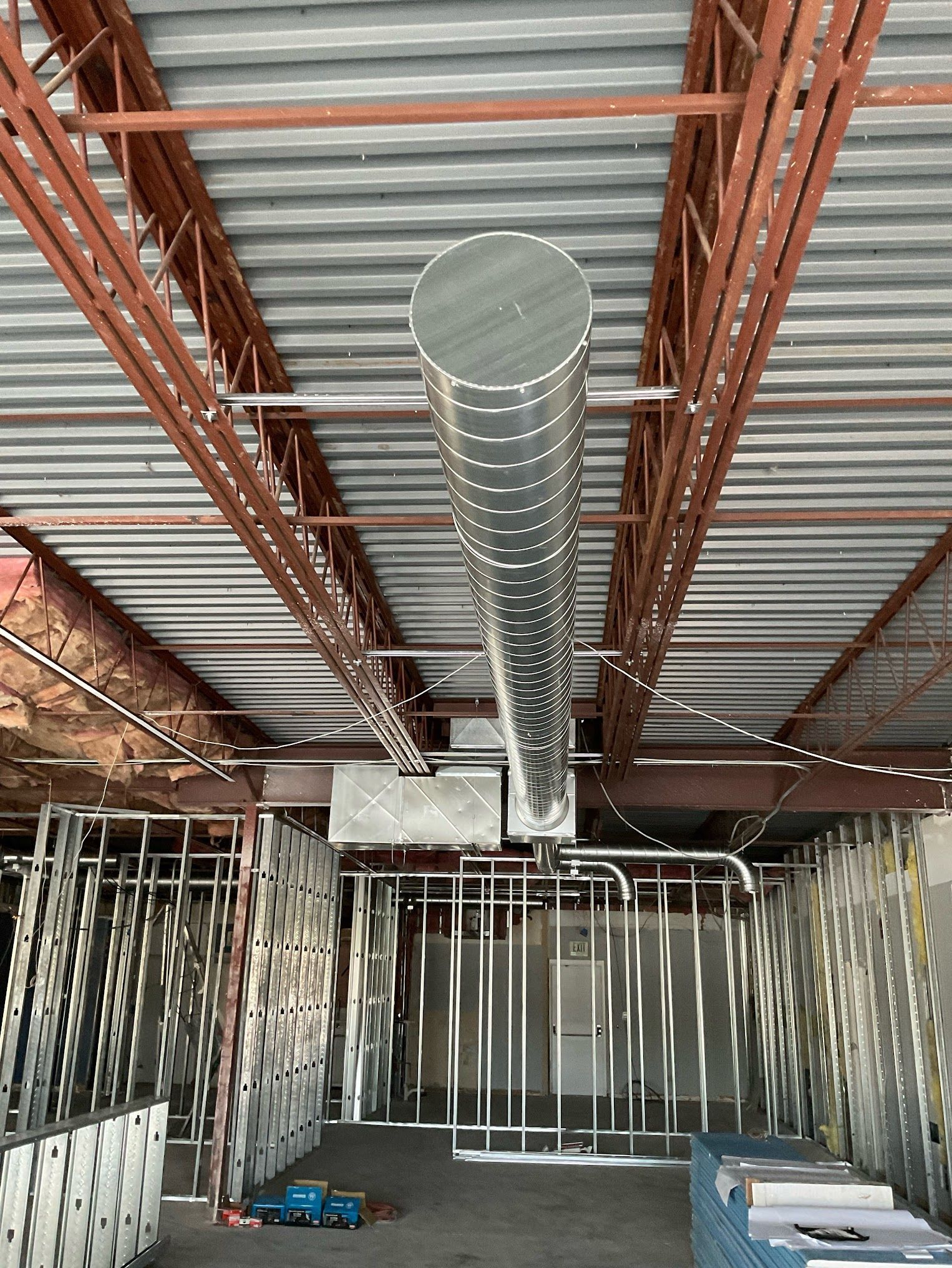 A large metal pipe is hanging from the ceiling of a building under construction.