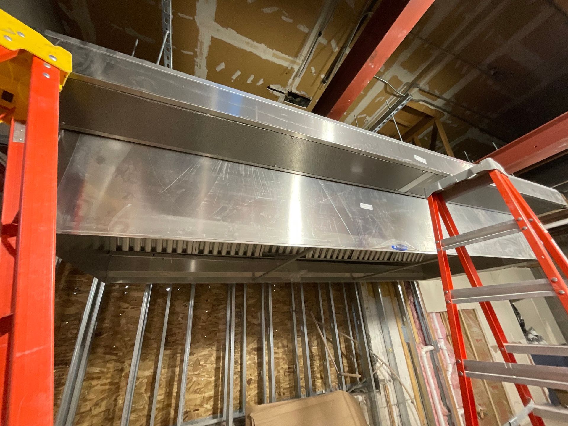 A red ladder is sitting next to a stainless steel exhaust hood in a building under construction.