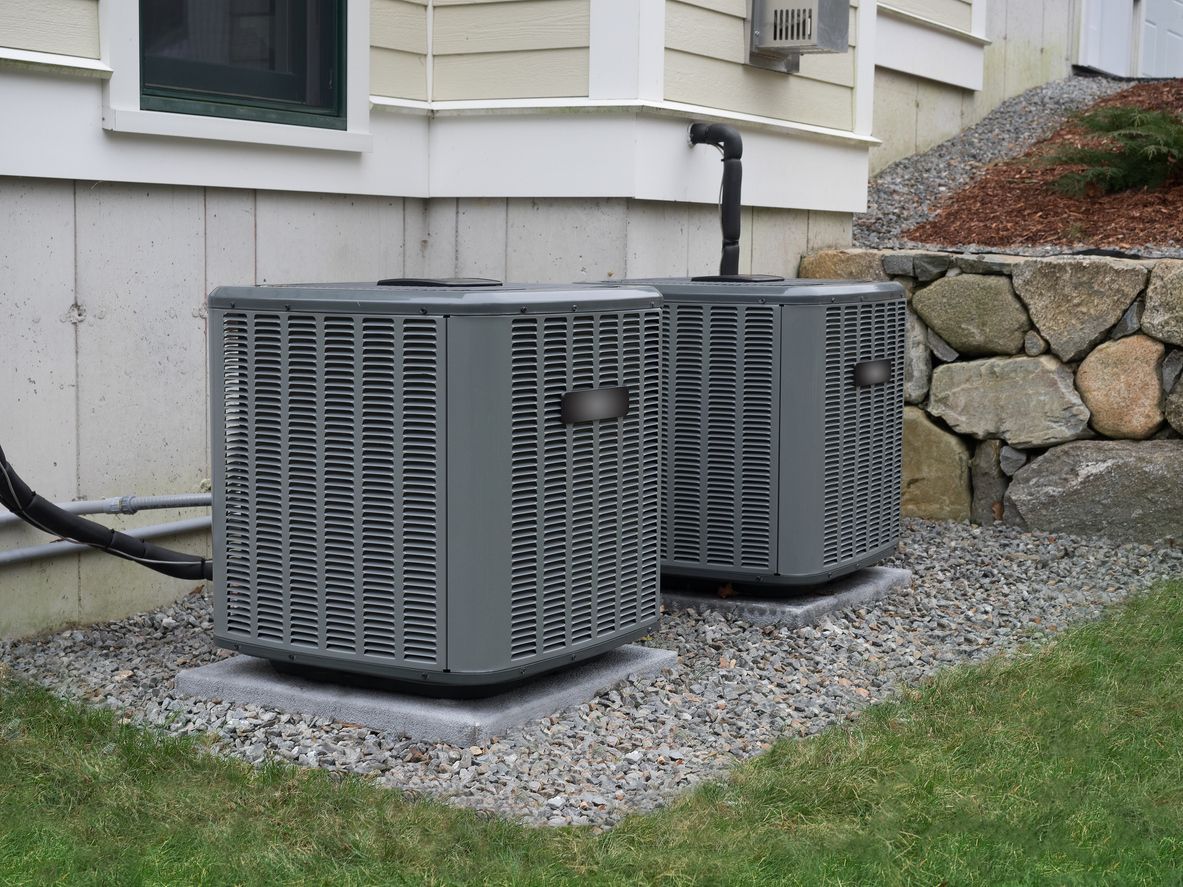 Two air conditioners are sitting outside of a house.
