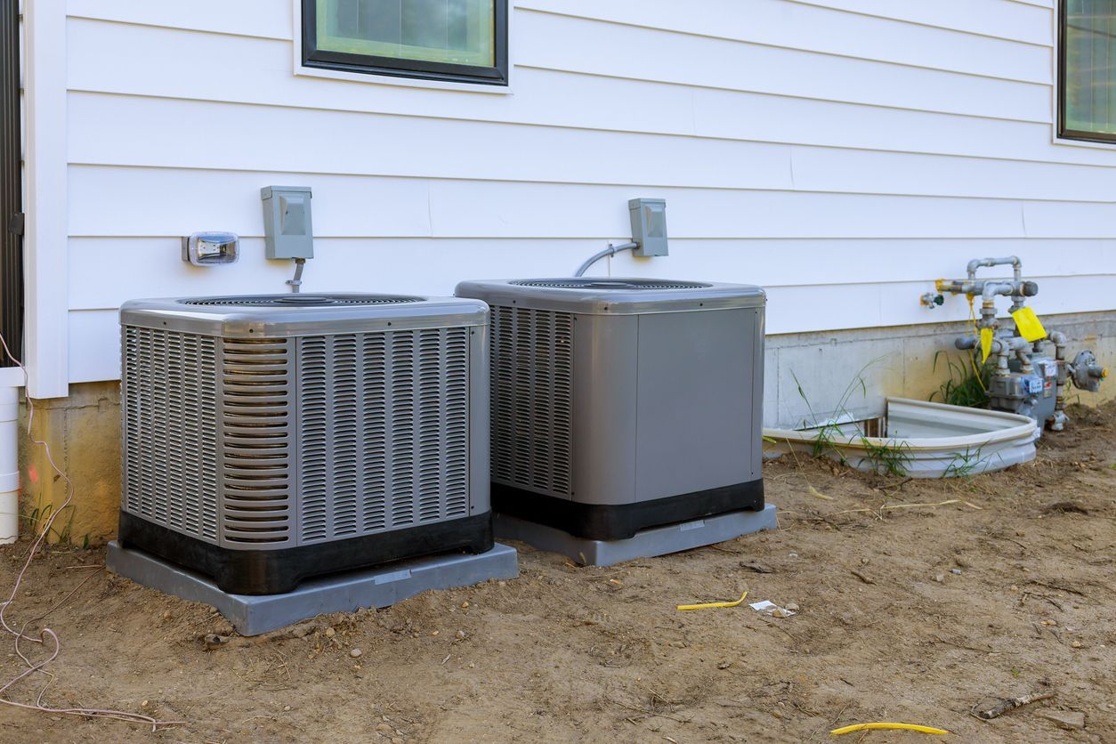 Two air conditioners are sitting on the side of a house.