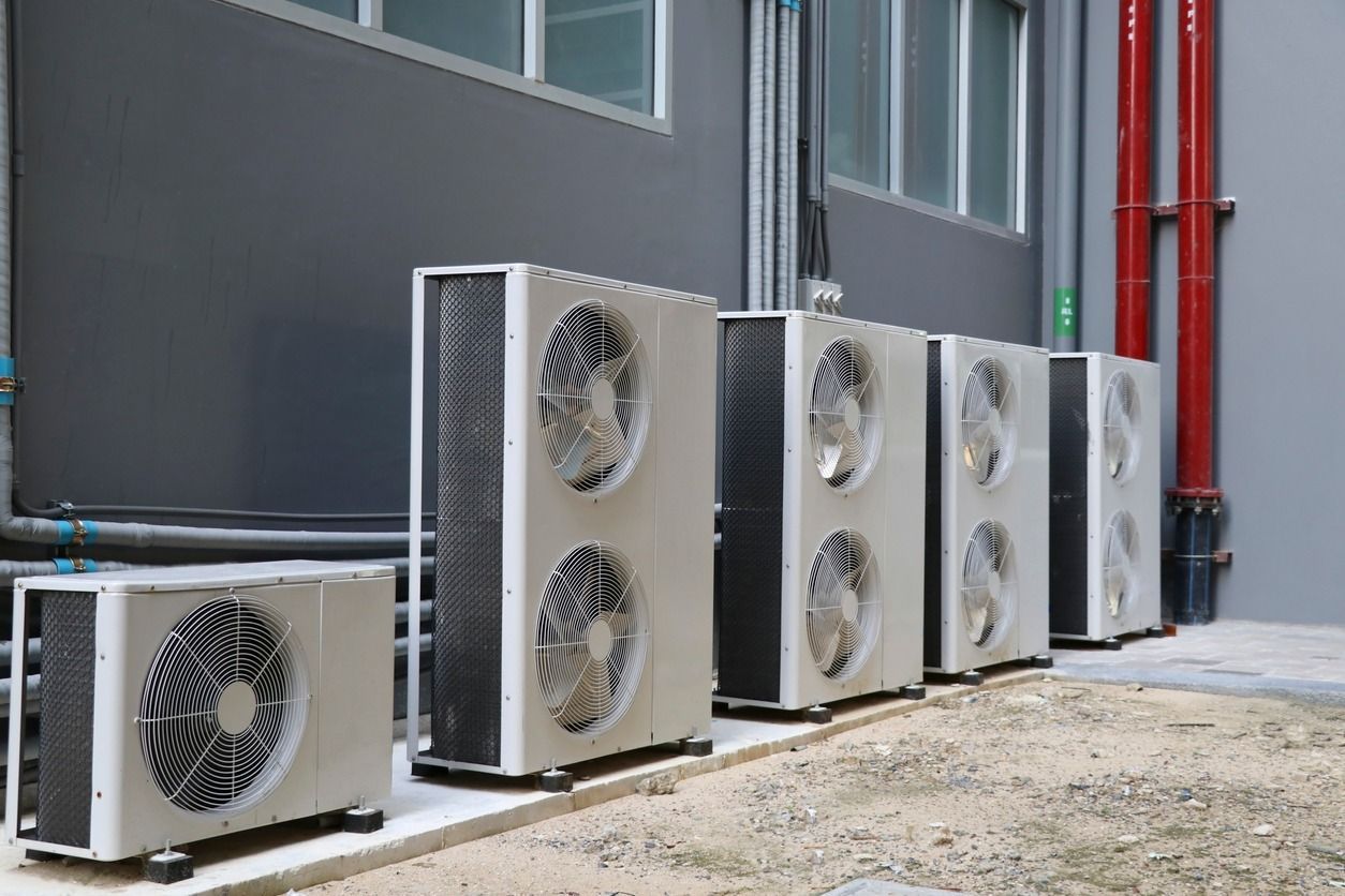 A row of air conditioners are lined up in front of a building.