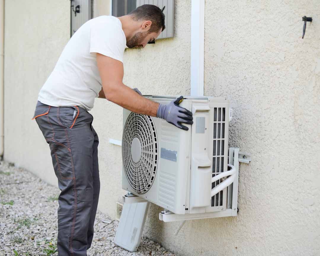 Two air conditioners are sitting next to each other on the side of a house.