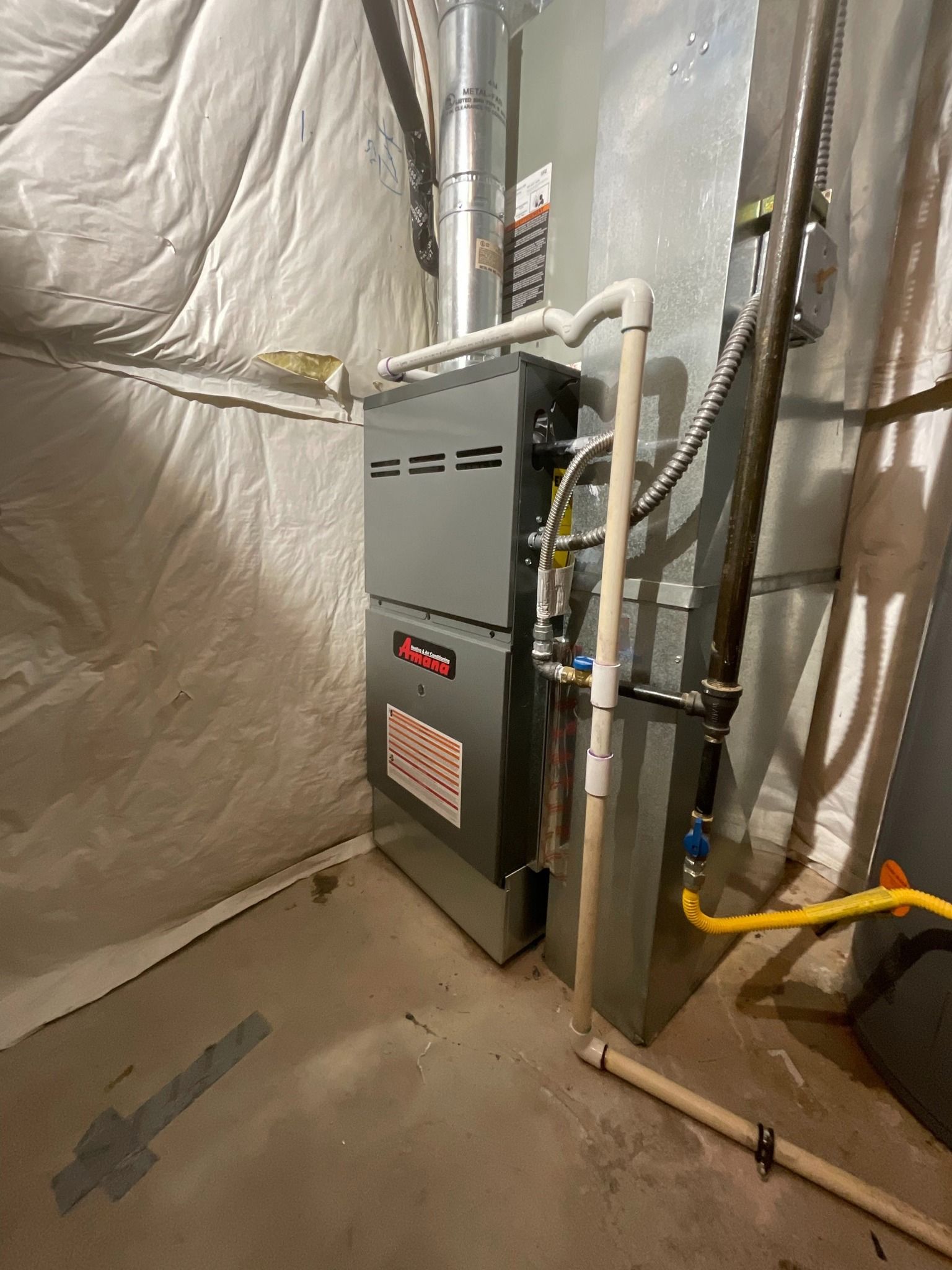 A gas furnace is sitting in a basement next to a wall.