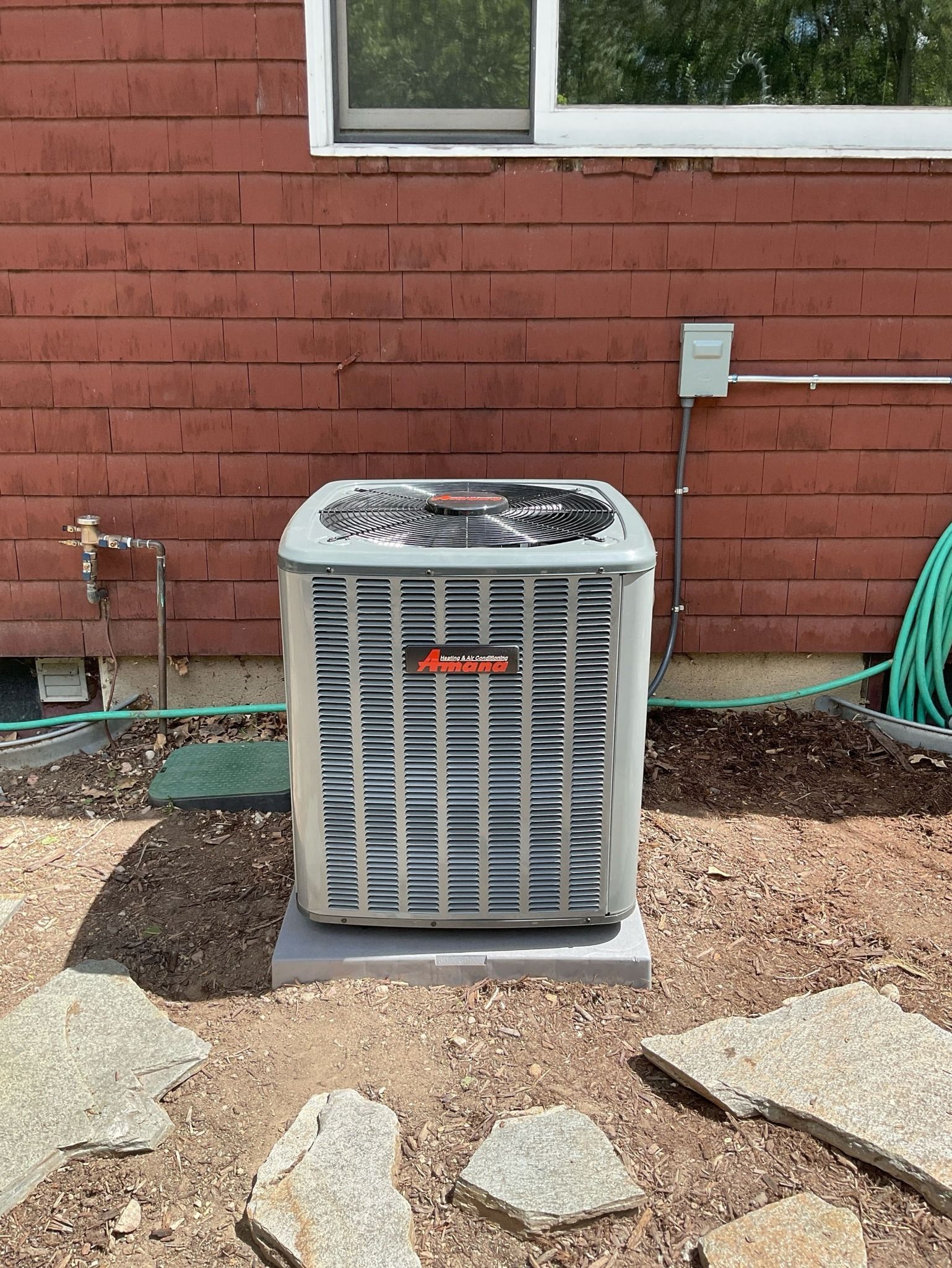 An air conditioner is sitting outside of a house next to a window.