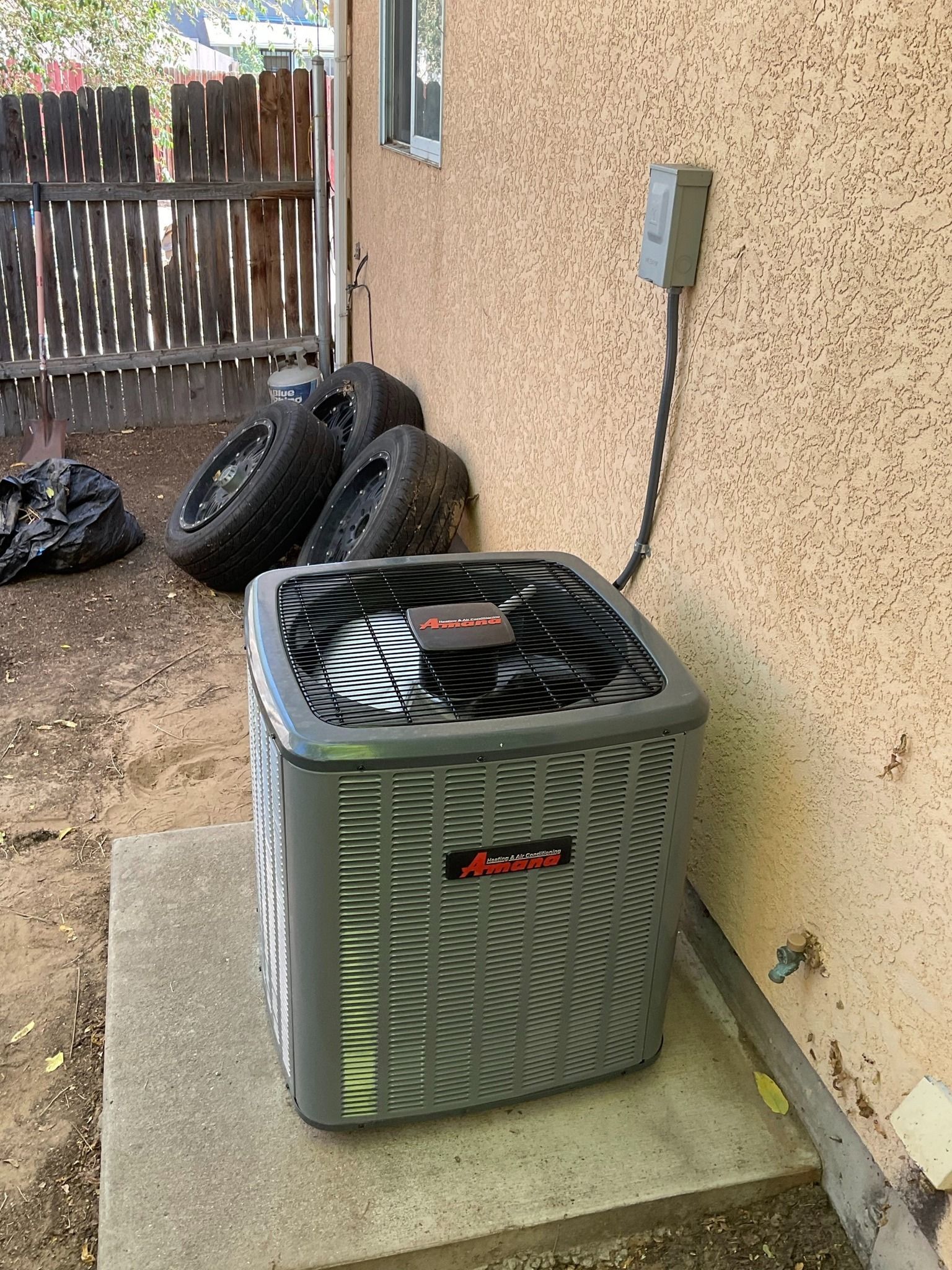 A gray air conditioner is sitting on a concrete platform in front of a house.