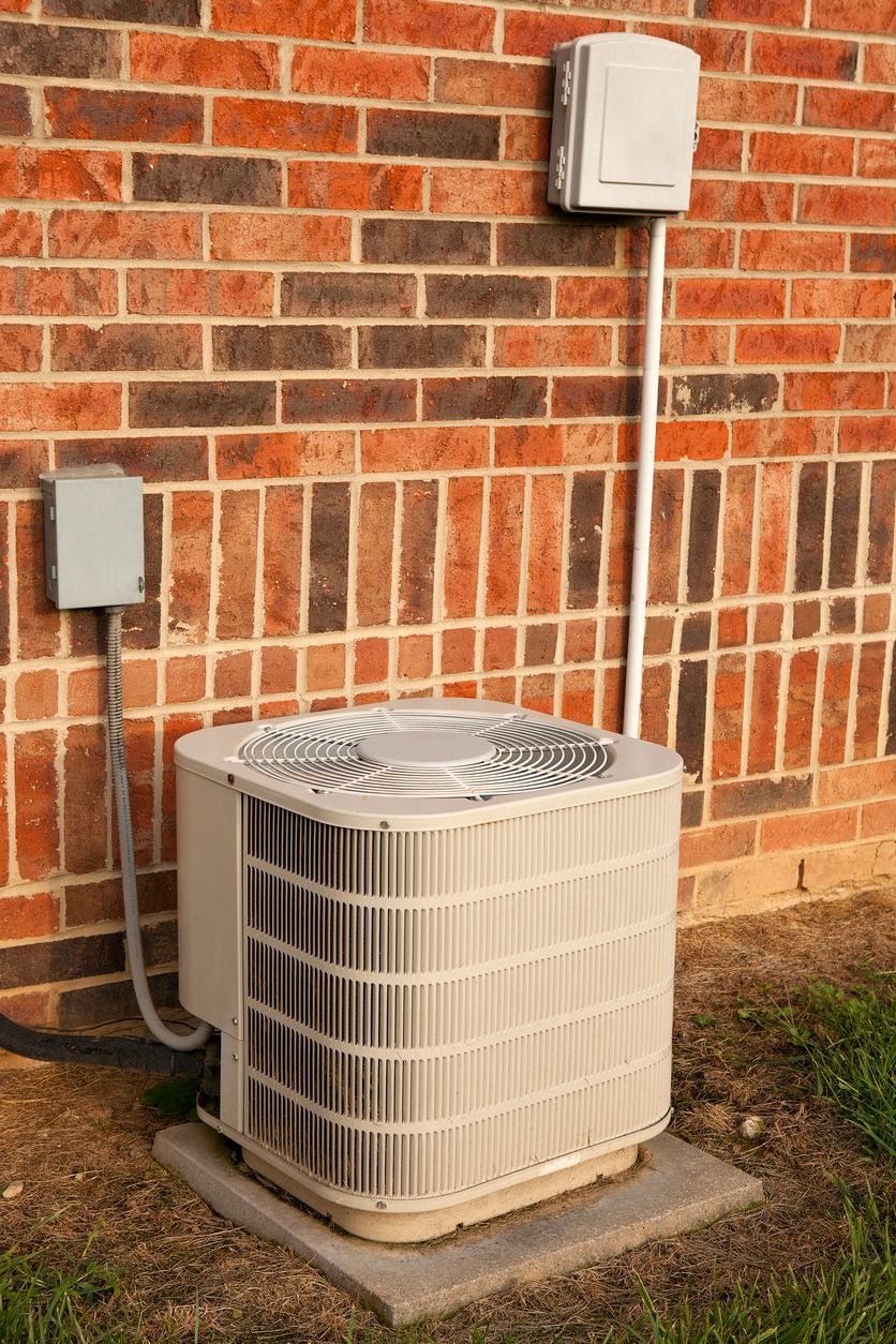 An air conditioner is sitting on the side of a brick building.