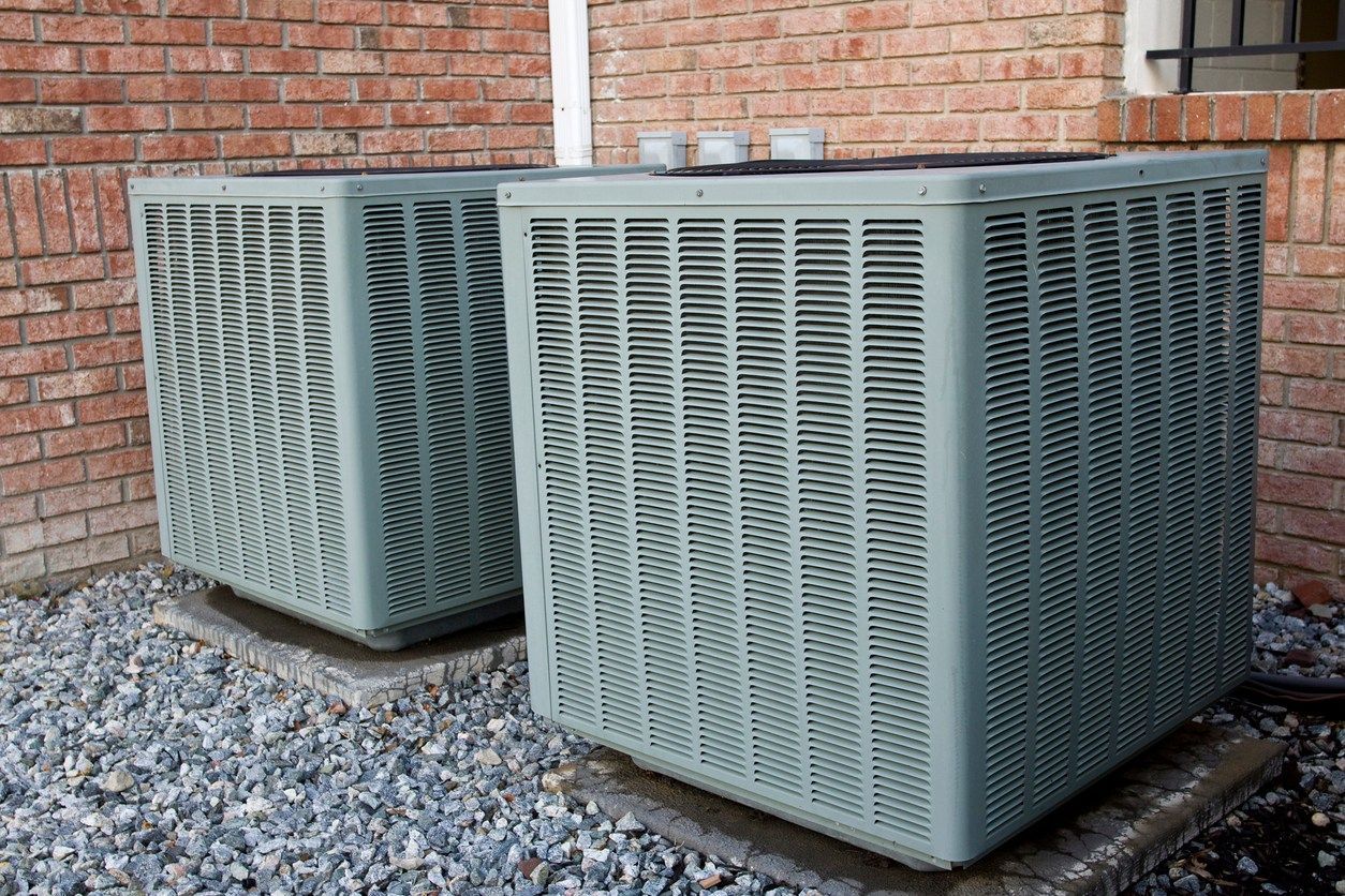 Two air conditioners are sitting on the side of a brick building.