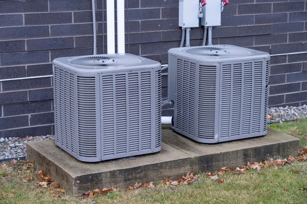 Two air conditioners are sitting on concrete blocks outside of a building.