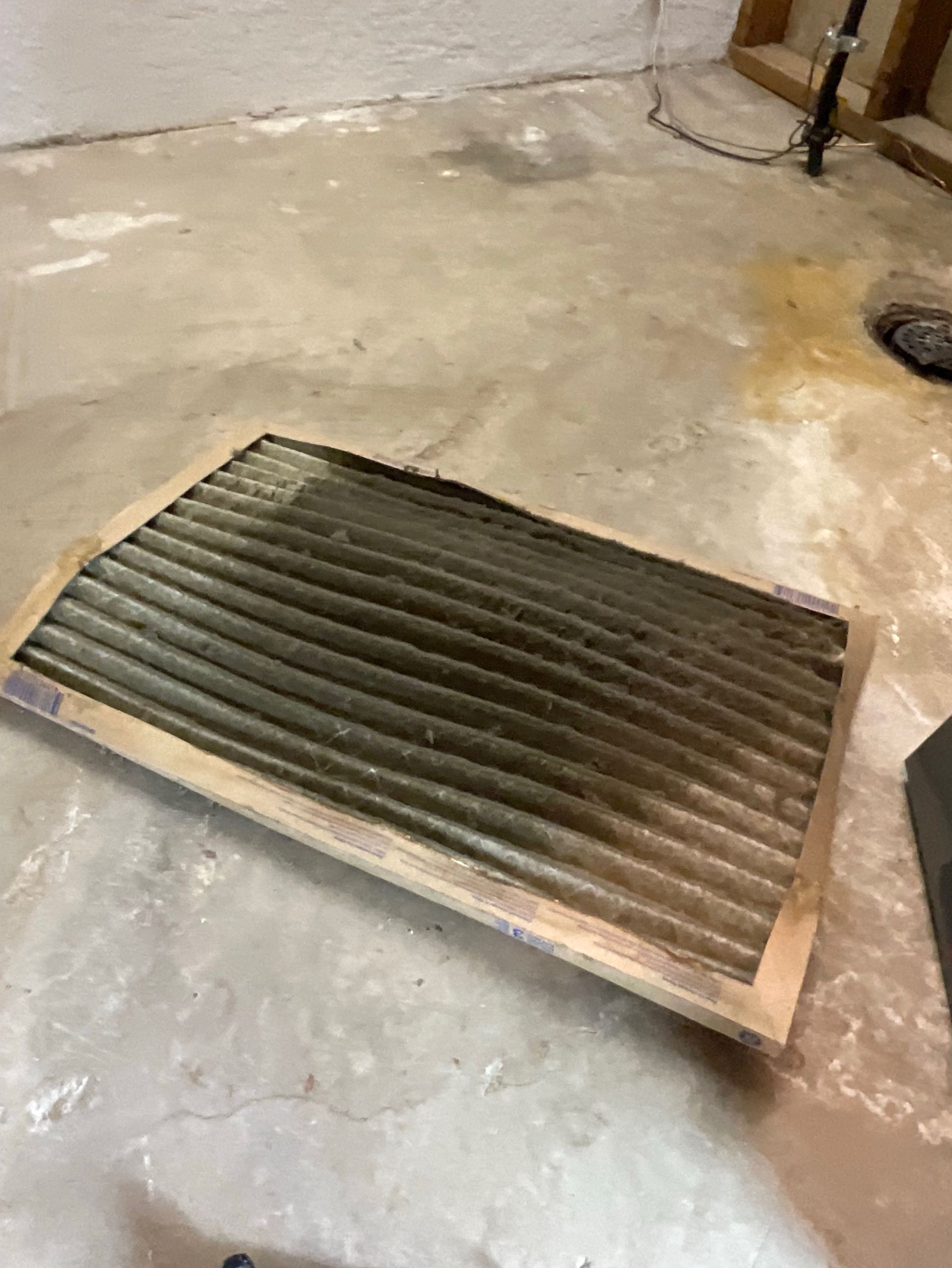 A dirty air filter is laying on the floor in a basement.