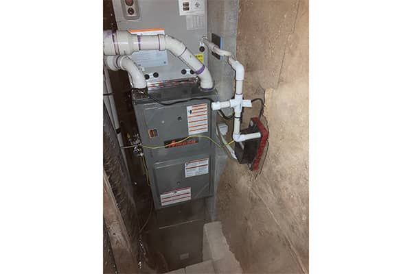 A furnace is sitting in a corner of a room next to a wall.