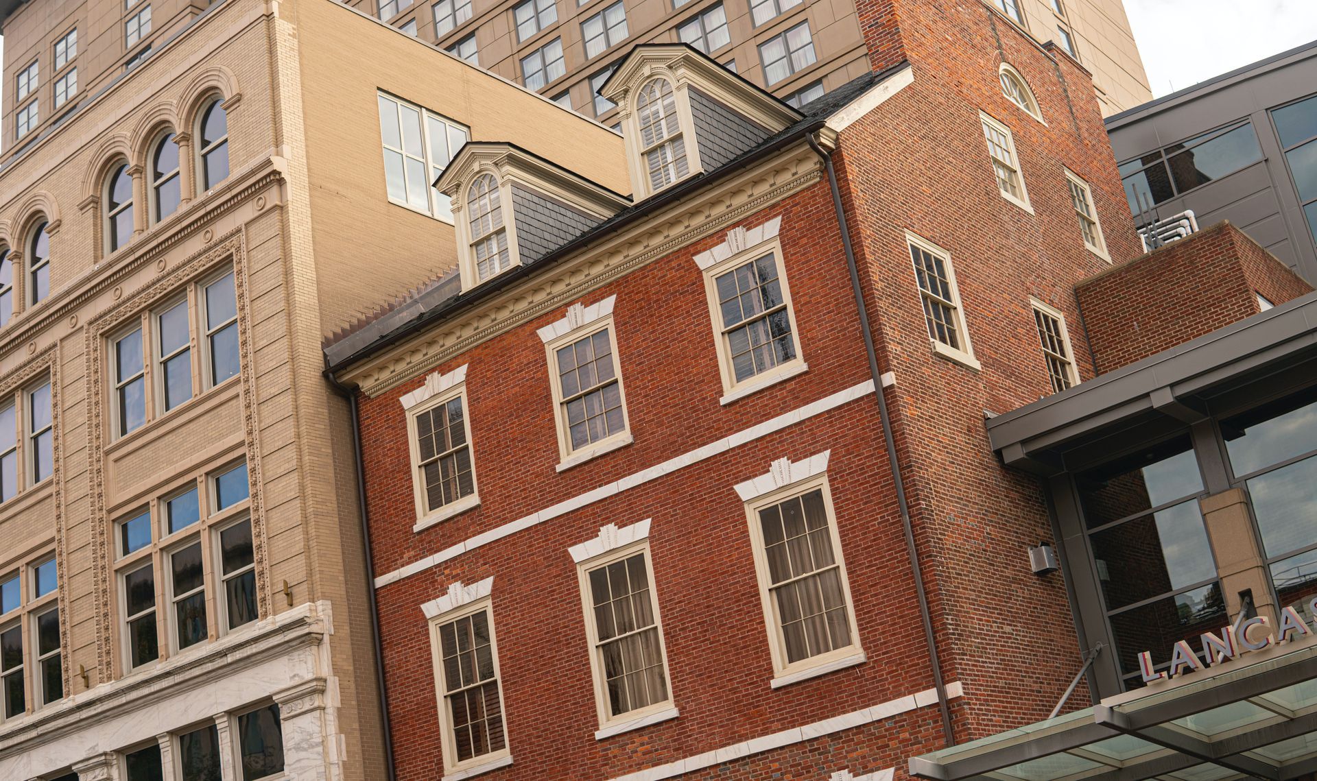 Red brick building wedged between taller modern buildings, contrasting styles.