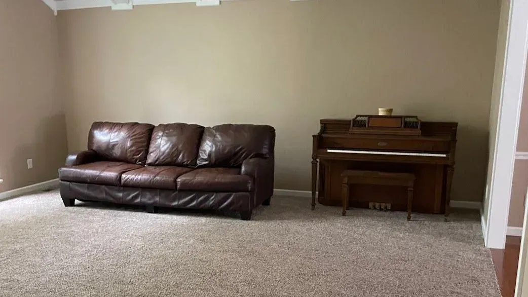 A brown leather sofa and a piano in a room with tan walls and carpet.