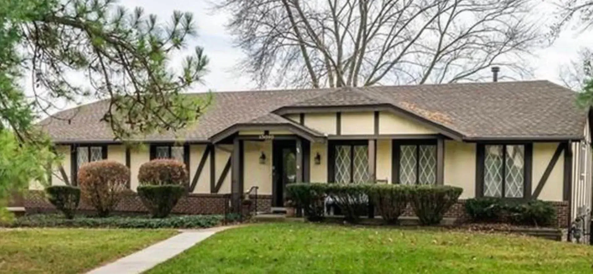 Tudor-style house with brown roof and trim, beige walls, and a green lawn.