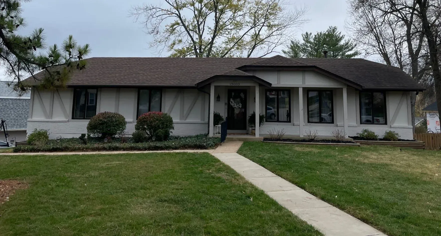 A white ranch-style house with a brown roof and a walkway leading to the front door, on a green lawn.