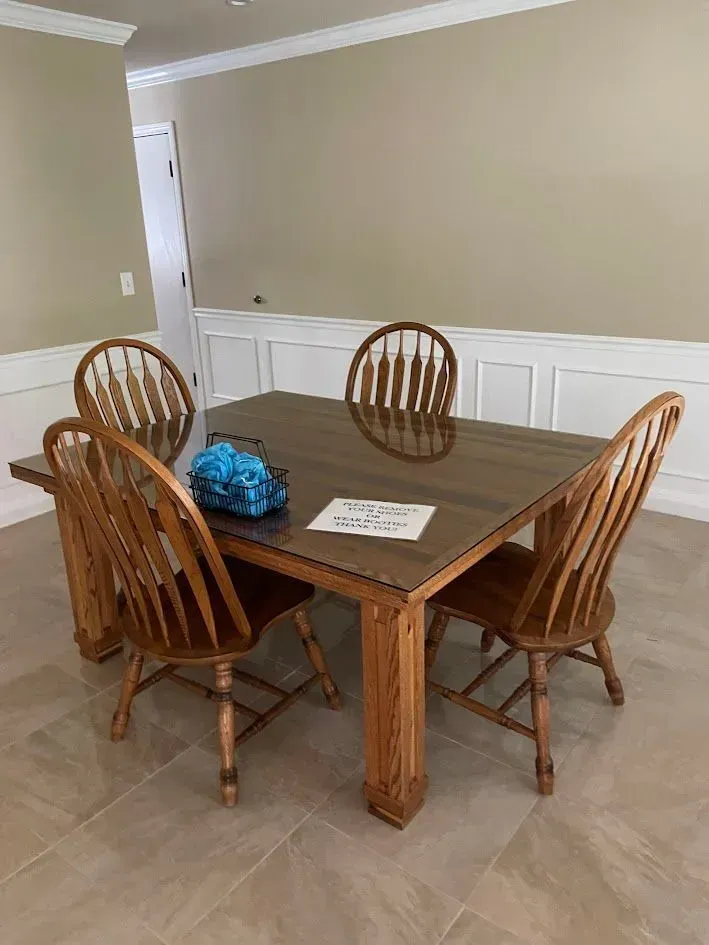 Dining room with wooden table and four chairs. Beige walls, white wainscoting, and light tile floor.