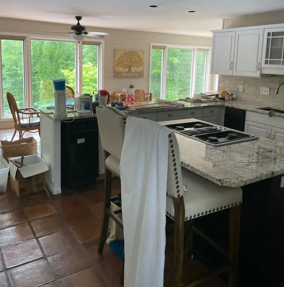 Kitchen with island, white cabinets, brown tile floor, and large windows overlooking trees.