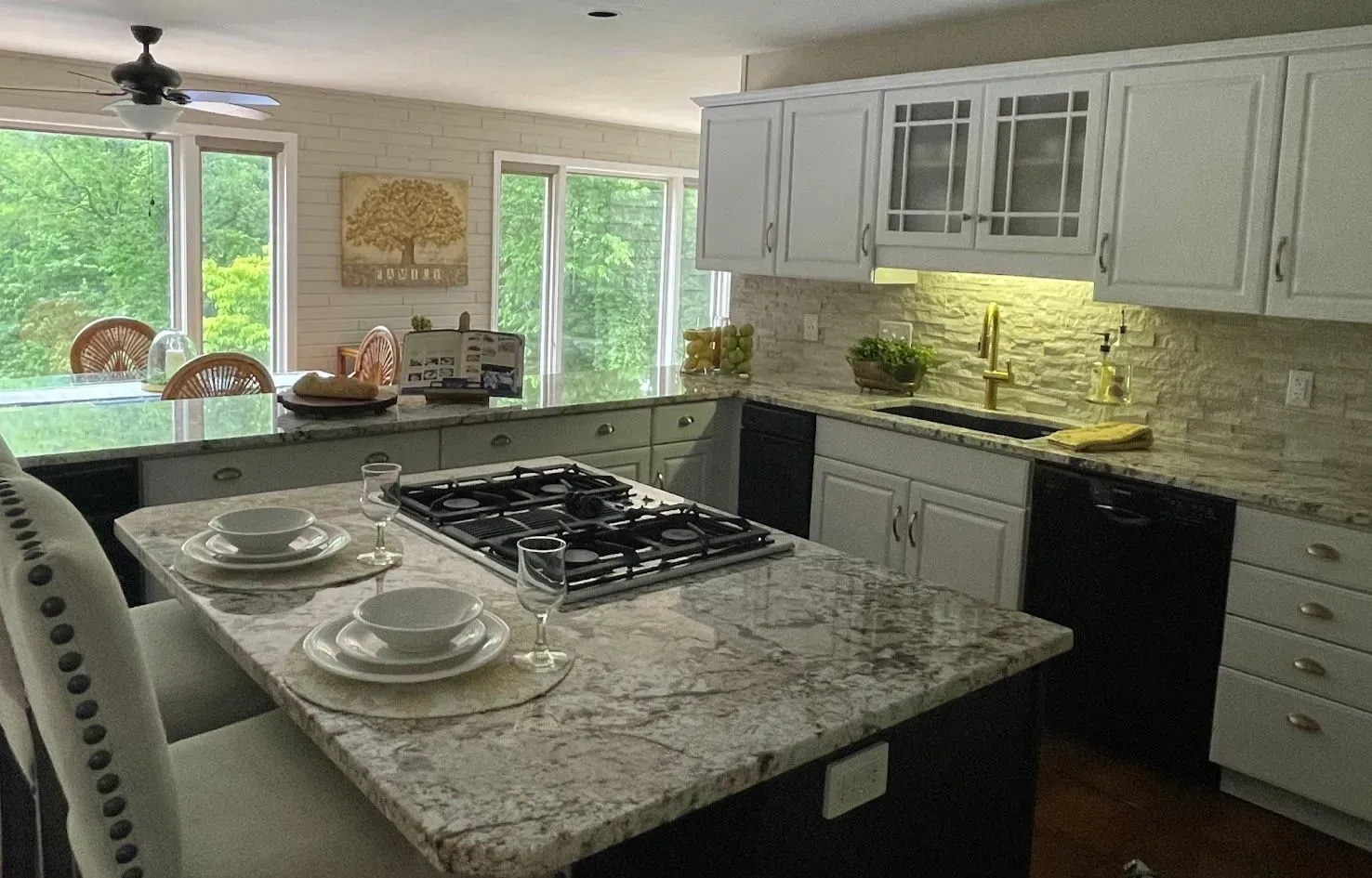 Kitchen with white cabinets, granite countertops, and a stovetop island; overlooking a backyard view.