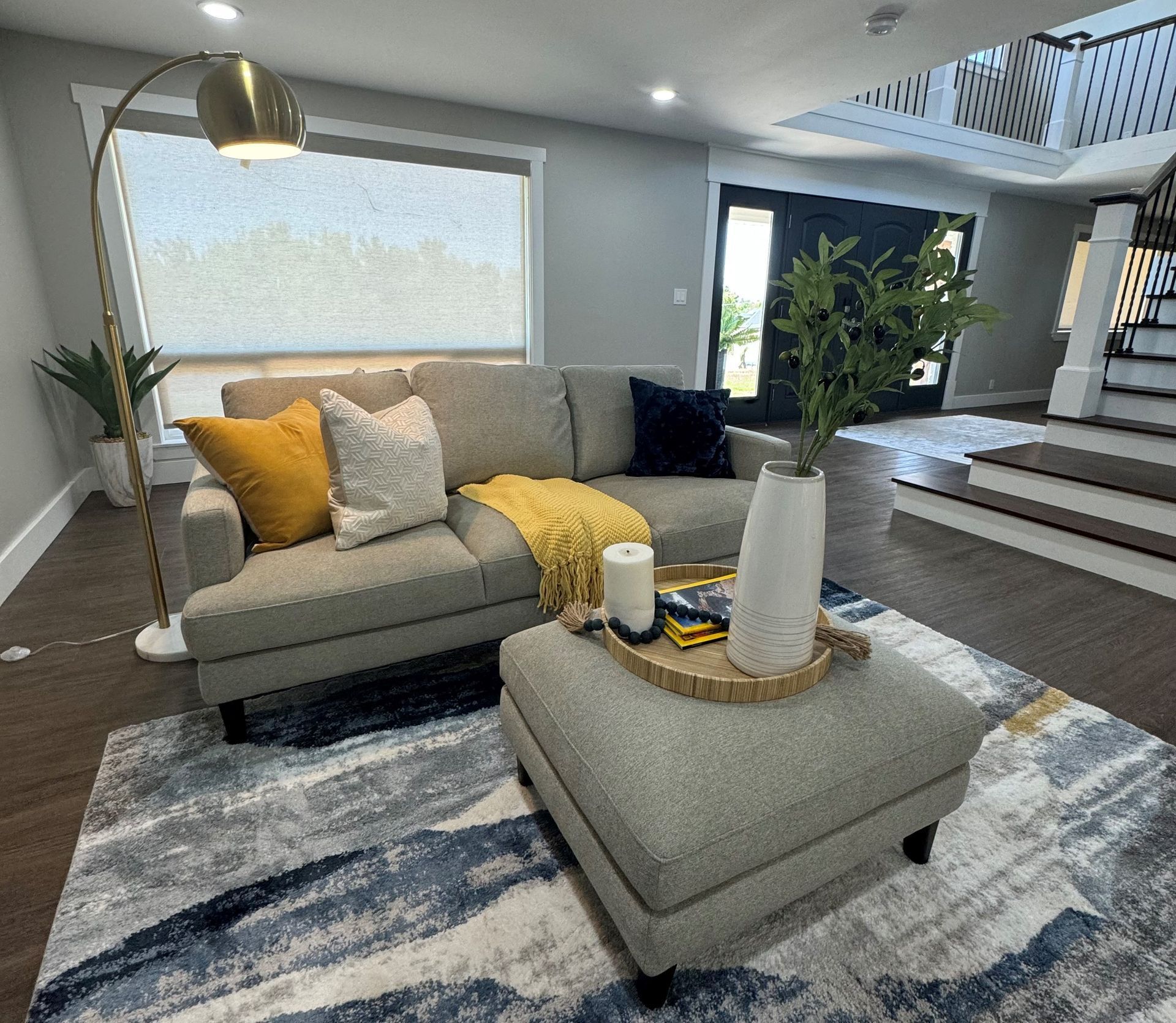 Living room with gray sectional sofa, ottoman, and area rug. Gold lamp and decorative pillows.