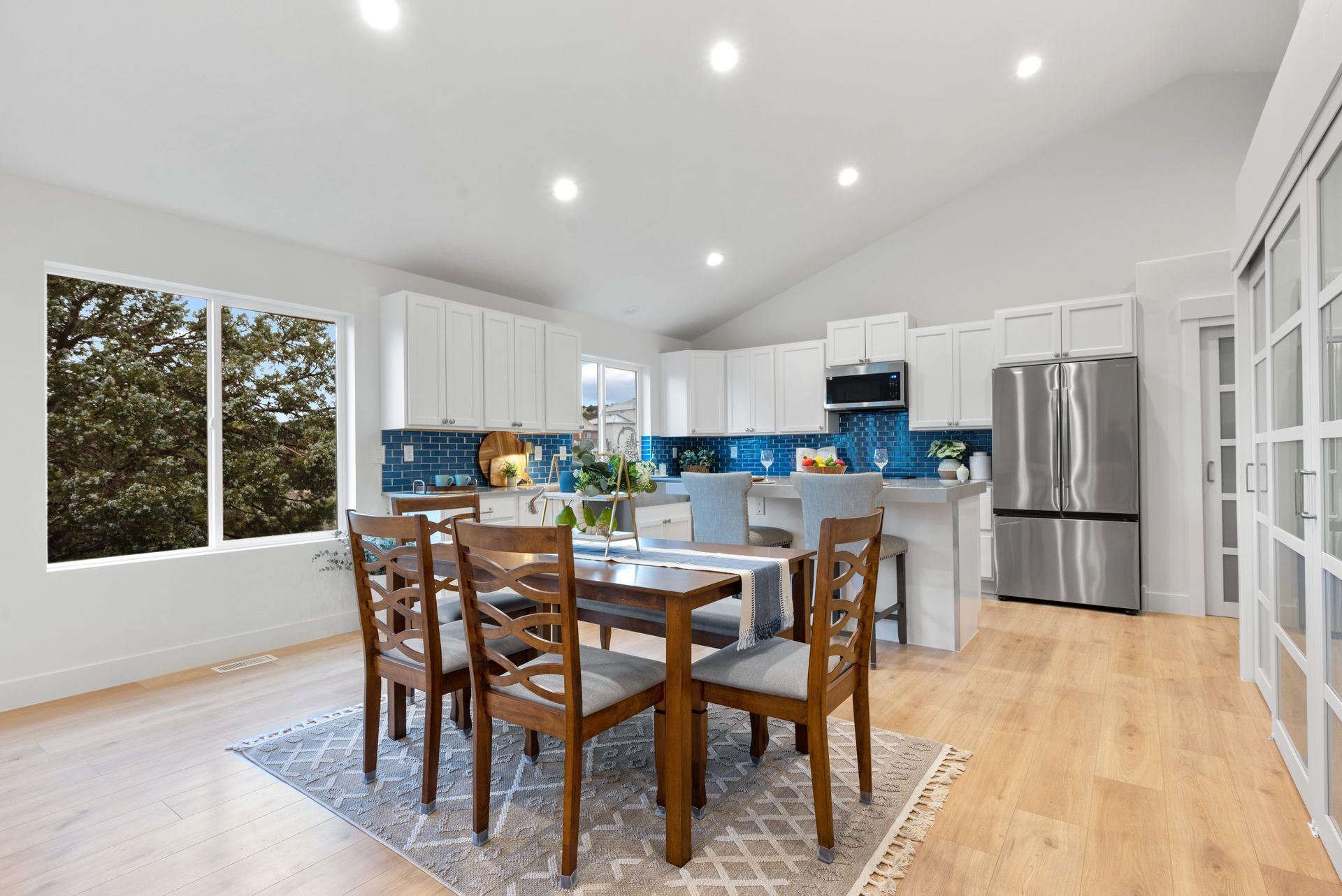 Bright kitchen and dining area with wood floors, white cabinets, and blue backsplash.